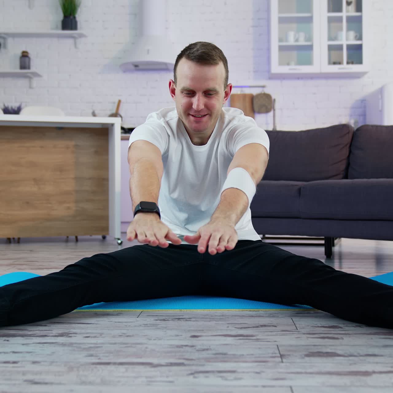 Young man doing workout at home. Guy is sitting on a mat and trying to do exercising during a quarantine period. Difficulties of doing workout at home