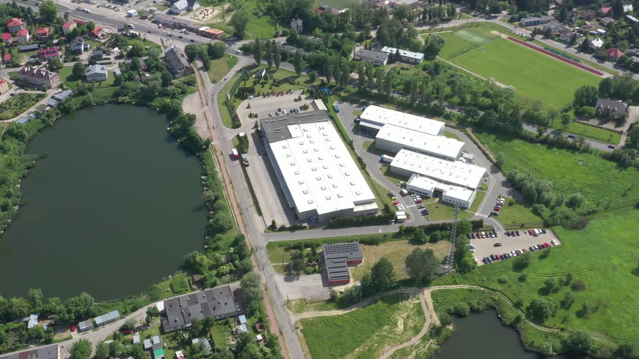 Ripresa aerea di un camion con semirimorchio che lascia un magazzino industriale, un edificio di stoccaggio o un'area di carico dove numerosi camion caricano e scaricano merci.