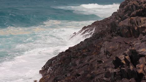 Tropical-ocean-waves-slowly-crashing-onto-rocks-on-the-Noosa-Heads-National-park-hike-in-Noosa-Heads,-Australia