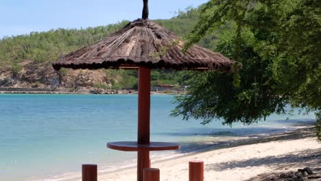 view of scenic picnic area with thatched roof sun parasol on white sandy beach in dili, timor-leste, southeast asia