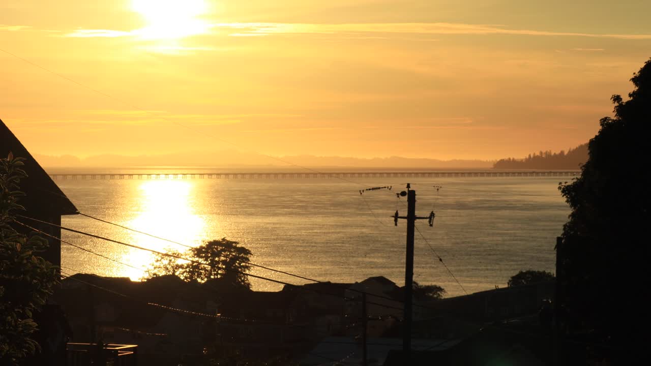 6월에 일몰 직전에 저속 황혼이 집과 나무 사이에 있는 오레곤의 컬럼비아 강 전망에서 낮은 다리와 워싱턴을 배경으로 하고 있습니다.