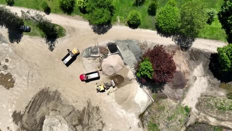 Excavator-moves-dirt-sand-from-top-of-pile-to-bottom,-aerial-top-down