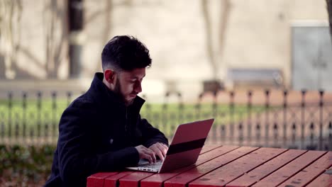 a young professional man doing typing work outdoors using his laptop - medium shot