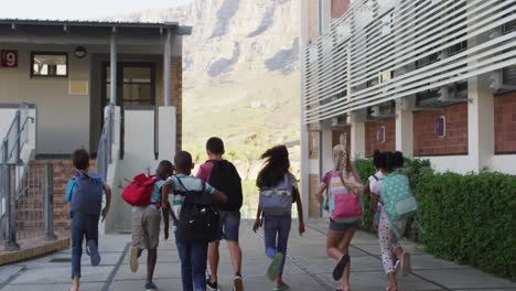 Diverse-group-of-happy-schoolchildren-wearing-backpacks-jumping-and-running-home-after-school