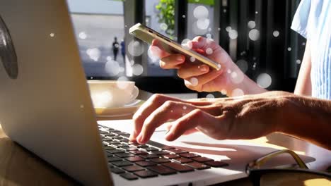 Animation-of-multiple-white-spots-over-midsection-of-woman-using-smartphone-and-laptop