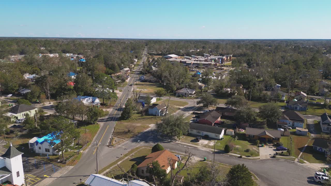 A Suburban Neighborhood Features Tree-lined Streets, Scattered Houses, and a Main Road Stretching Into the Distance - Aerial Drone Shot