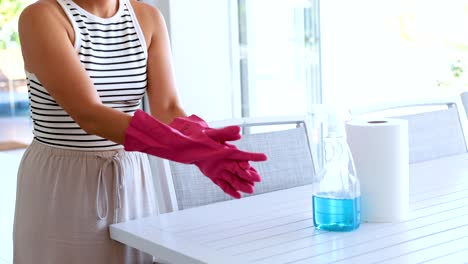 a woman in a striped top puts on pink rubber gloves in a bright kitchen setting