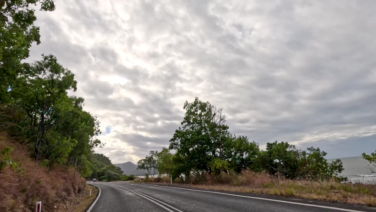 A serene drive through lush greenery and coastal views under overcast skies in Port Douglas, Queensland