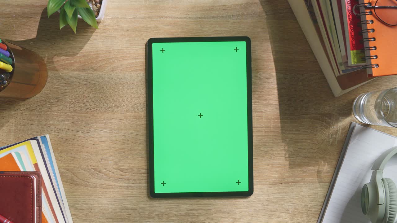 vista de arriba hacia abajo de una computadora portátil con pantalla verde simulada pantalla chromakey en un escritorio de oficina de madera al lado de la libreta con bolígrafos, gafas y un vaso de agua.