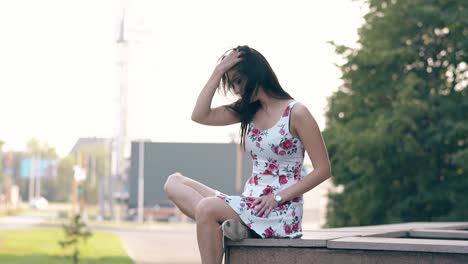 girl in coloured summer dress sits on ceramic barrier