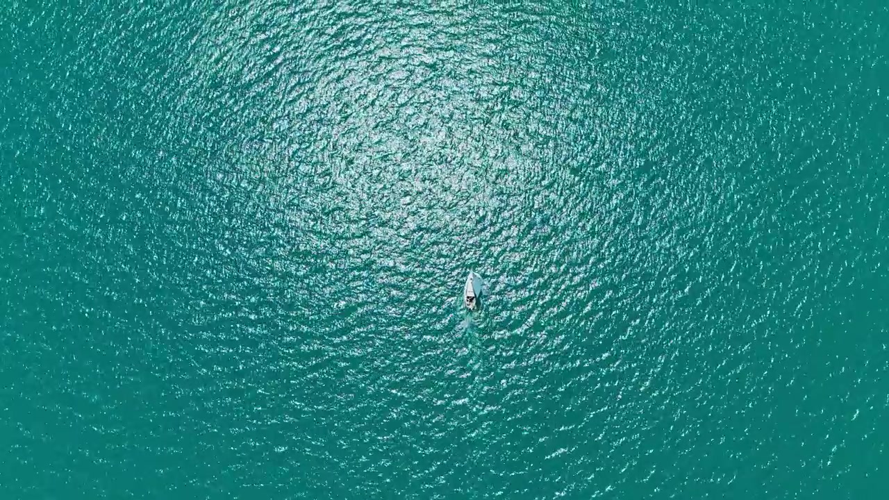 Sailboat floats on bright blue waters under a clear sky during a sunny day at sea near the coastline