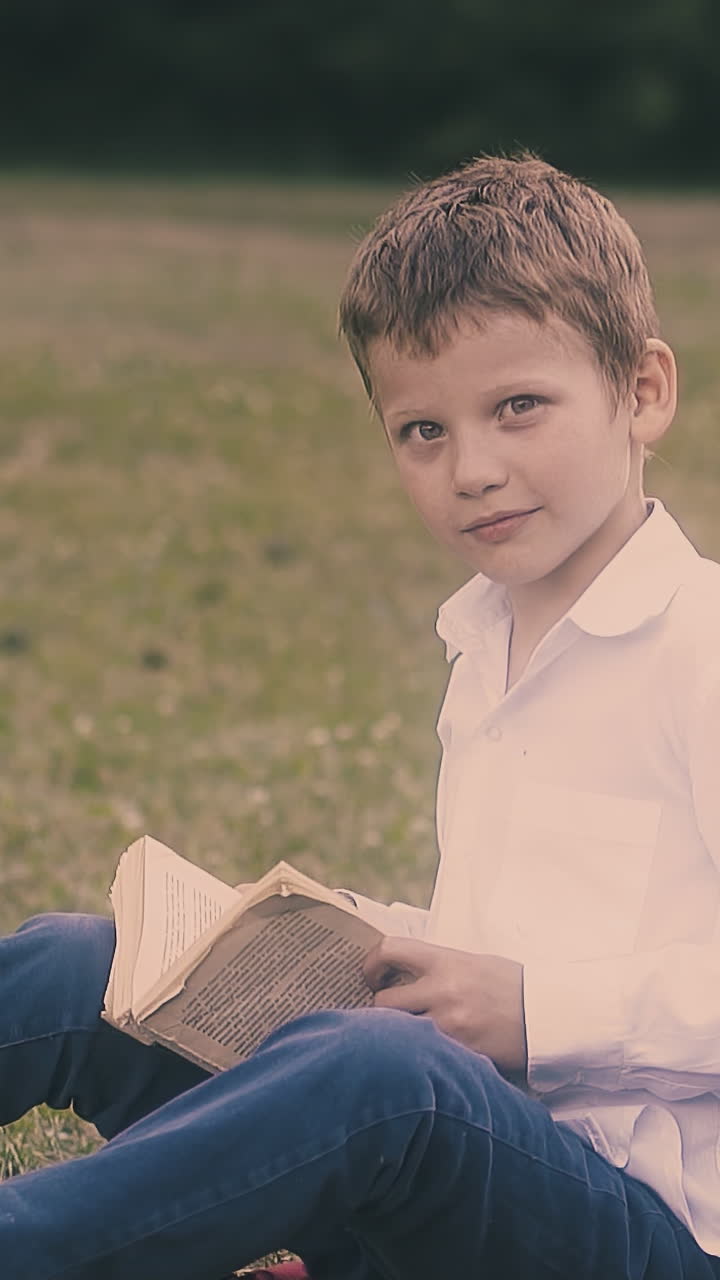 concentrated boy in white shirt sits in green school garden back to schoolmate back sleeping with book slow motion