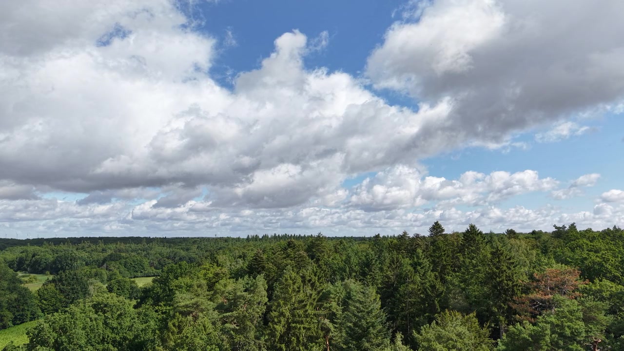 Time-lapse view of dramatic clouds drifting over a vast green forest landscape beneath a blue sky, capturing the beauty of nature, changing weather, and peaceful wilderness from above.