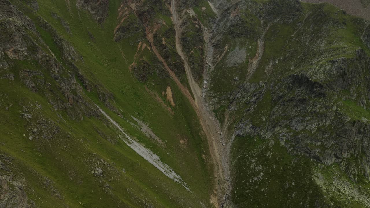 Rugged green and rocky mountainside at Umbrail Pass in Swiss Alps, alpine terrain, scree slopes, and natural erosion. Aerial drone
