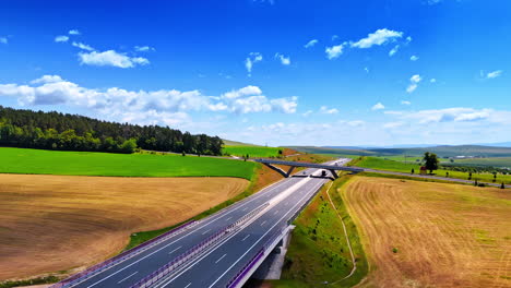 Sunny road through green fields. Trucks and cars travel along a wide highway surrounded by vibrant green fields and blue skies