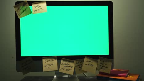 close up of modern working place with a chromakey screen computer, daily planners and post it notes. concept. female hand glueing a sticker note on a computer with green screen