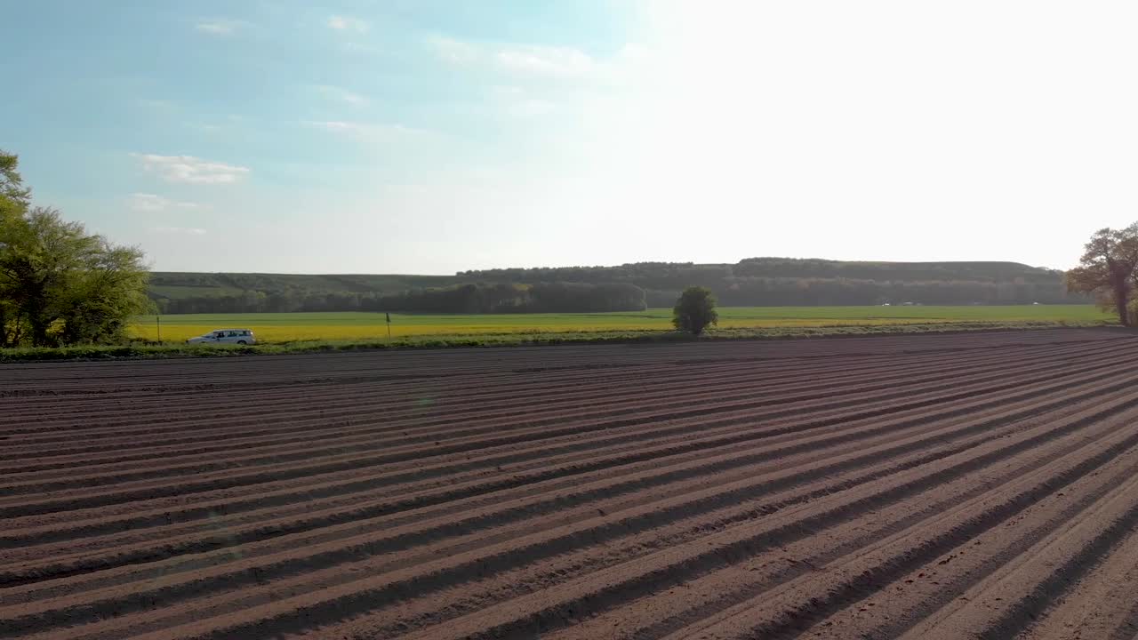 Herabsteigende Drohnenaufnahme über frisch bewirtschafteten Feldern in der englischen Landschaft an einem sonnigen Sommernachmittag mit gelben Pflanzen