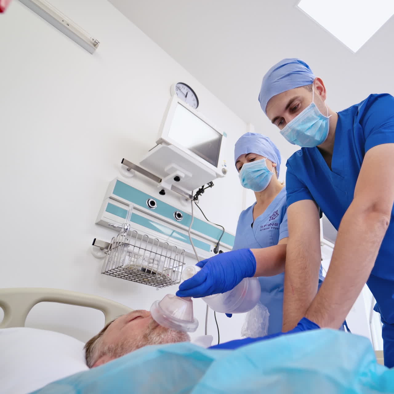 Unconscious man patient laying on bed and specialist giving resuscitation. View from below on a doctor and nurse saving patient's life in the light emergency room.