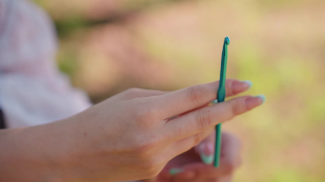 Close up of woman hands holding and examining various blue crochet hooks in soft natural light. focus remains on texture detail shape variations between different sized tools with background