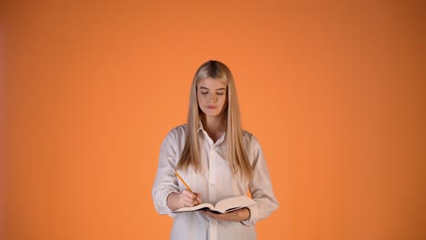 joven rubia escribiendo notas en un cuaderno, pensando y encontrando una idea inteligente, colorida toma de estudio