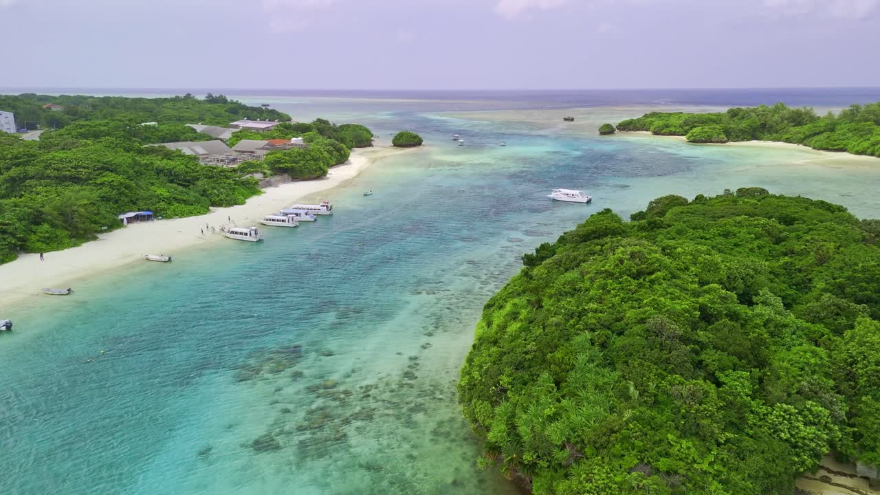 An aerial view of tourist boats and a rocky islet covered in green trees, floating in the clear turquoise waters of Kabira Bay in Ishigaki, Japan