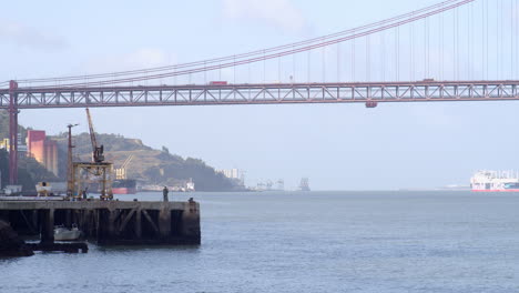 fisherman at almada's sea break with lisbon bridge at the end of the frame