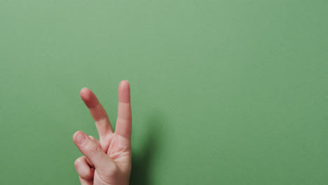 Close-up-of-hand-of-biracial-man-showing-peace-sign-with-copy-space-on-green-background