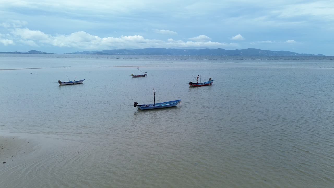 Drone footage capturing small fishing boats anchored off Koh Phangan, Thailand, with the open ocean stretching towards the distant island of Koh Samui