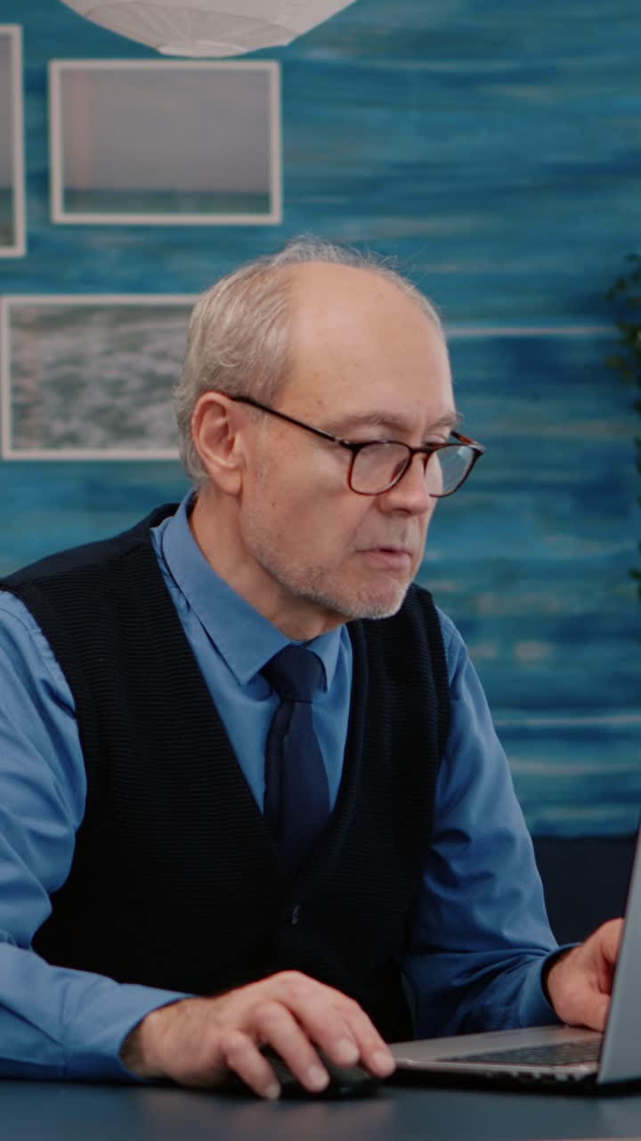 Vertical video: Old freelancer typing on laptop sitting in living room working remote