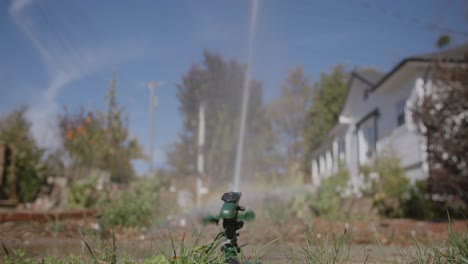 Breite-Aufnahmen-Von-Der-Rückseite-Eines-Sprinklers,-Der-Einen-Garten-Mit-Einem-Kleinen-Regenbogen-Bewässert