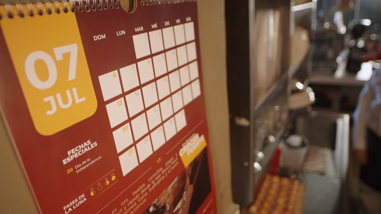 Close-up view of a wall calendar showing daily notes in a busy bakery kitchen.
