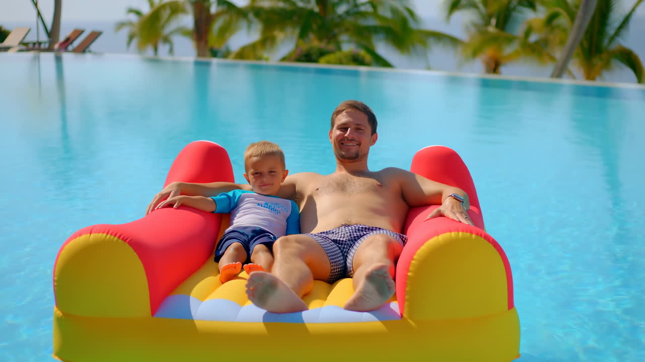 Father and Son Relaxing on Inflatable Float in Infinity Pool