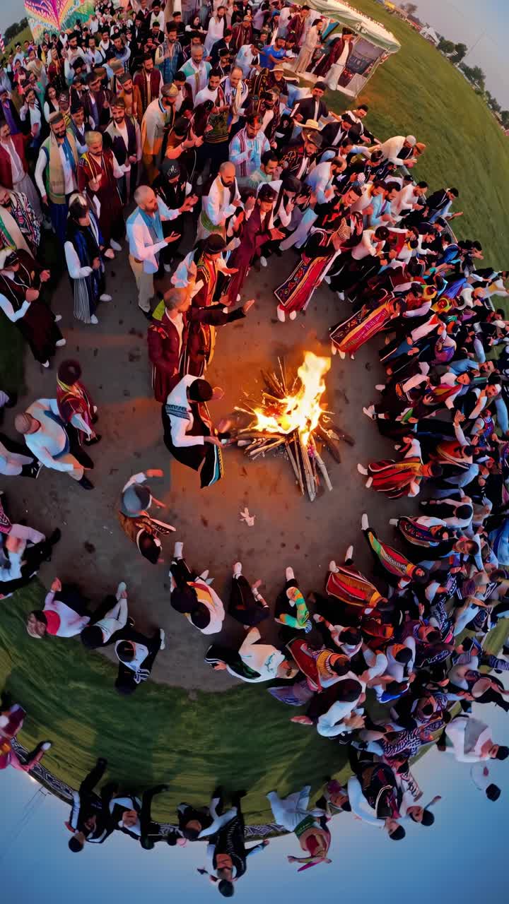 Aerial view of a large group of people wearing traditional costumes celebrating a festival, dancing around a bonfire with a little planet effect applied to the image