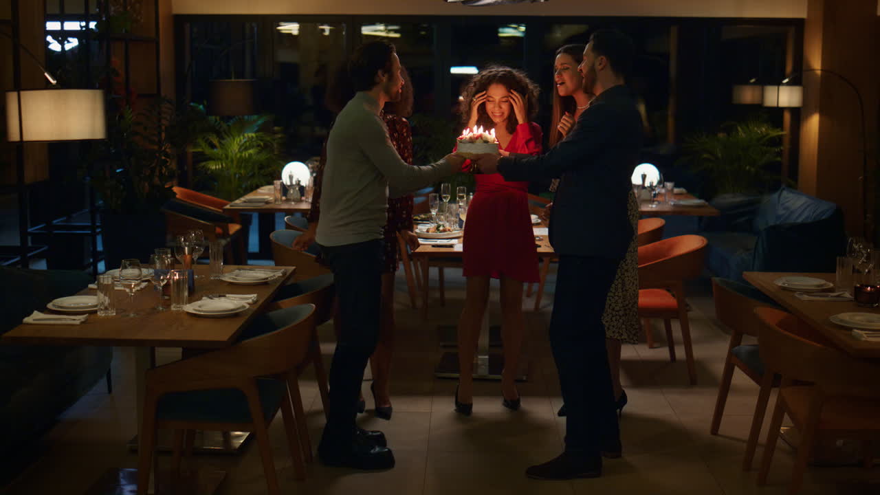 mujer sorprendida soplando pastel en la fiesta de cumpleaños. amigos celebran en el restaurante.