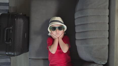 adorable toddler adjusts straw hat lying on soft grey sofa