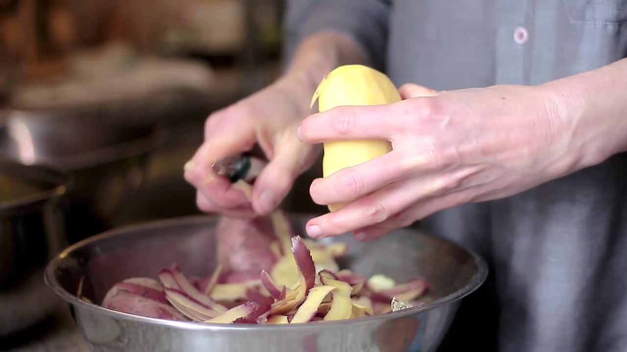 peeling potato with a knife in a bowl in the kitchen with people stock video stock footage