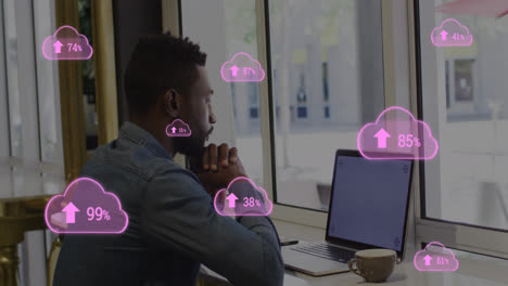 Animation-of-pink-clouds-with-rising-numbers-and-businessman-using-laptop-in-office