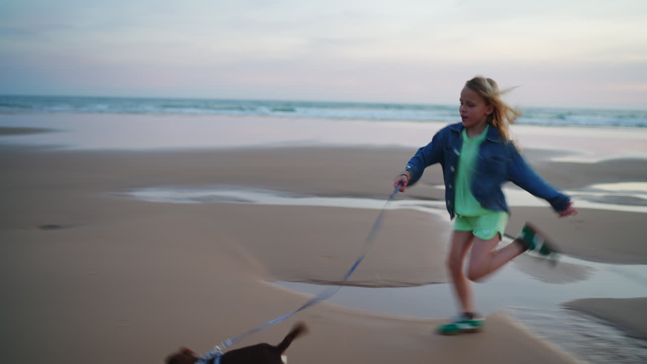 Niña corriendo con su perro en una playa de arena al atardecer.