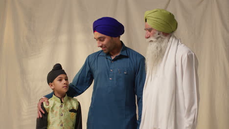 studio shot of multi generation male sikh family wearing turbans standing against plain background