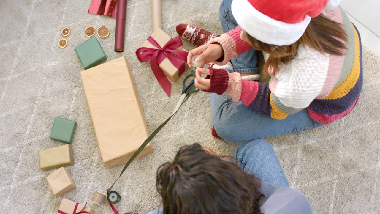 Checking phone couple decorating gift bow threading orange slice with ribbon on living room rug