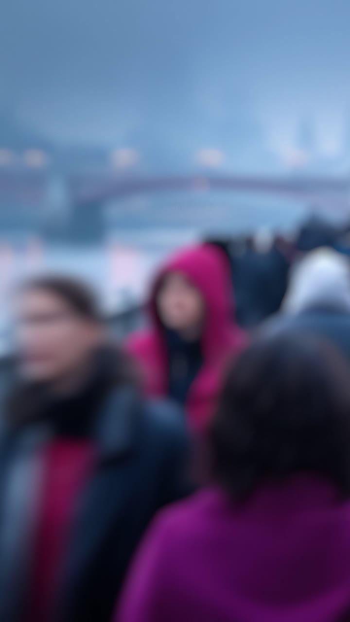 Un gruppo di figure sfocate che camminano lungo un lungomare, creando un'atmosfera misteriosa in un paesaggio urbano sotto cieli nuvolosi e una fioca illuminazione atmosferica