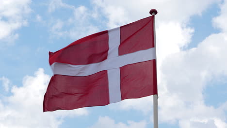 national flag of denmark waving against bright blue sky with clouds