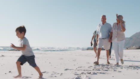 Familie-Mit-Mehreren-Generationen-Spaziert-Im-Sommerurlaub-Am-Sandstrand-Entlang