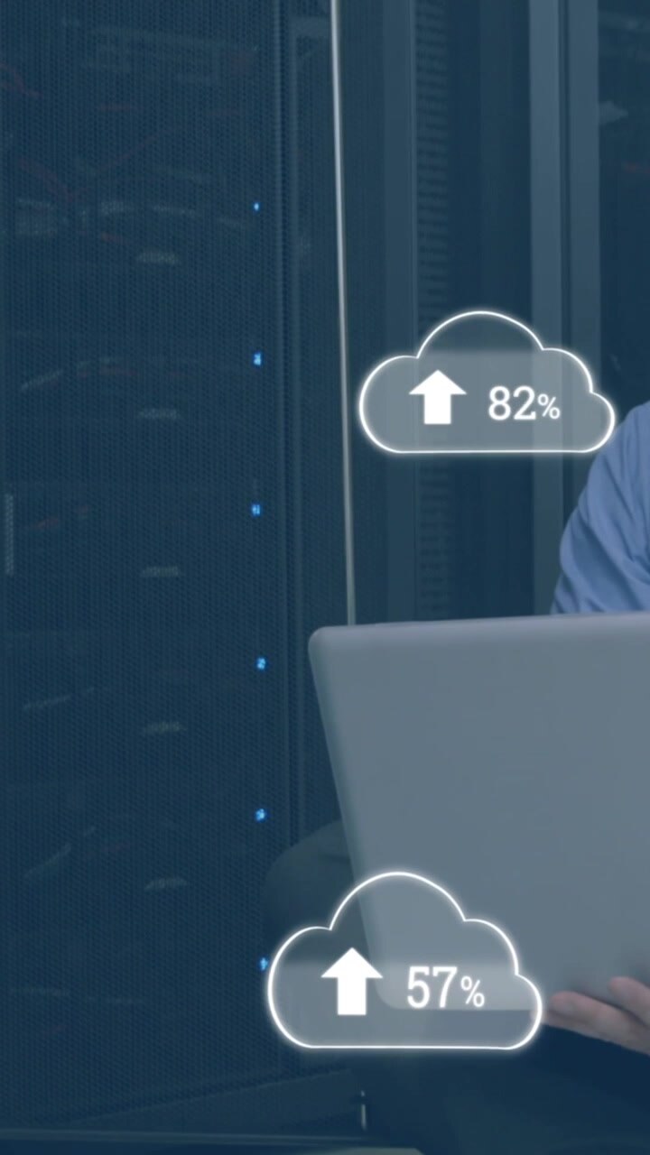 Animation of clouds with numbers over stressed caucasian man working on laptop in server room