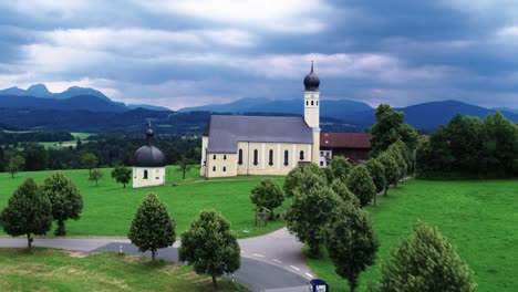 toma aérea de la iglesia de peregrinación wilparting con nubes impresionantes y vuelo hacia los alpes con el monte wendelstein en la parte posterior, baviera, alemania