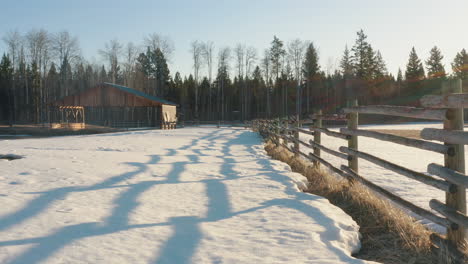 Smooth-glide-along-farm-fence-over-snowy-ground-at-sunrise