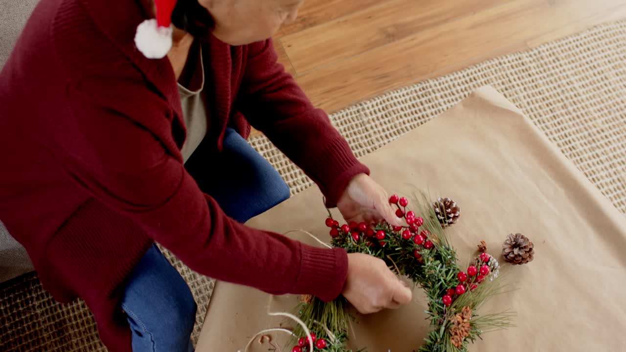 Decorating Christmas wreath with pinecones, senior woman crafting at home