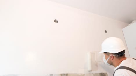a young man in a construction helmet paints the walls in an apartment a young man in a construction helmet paints the walls in an apartment