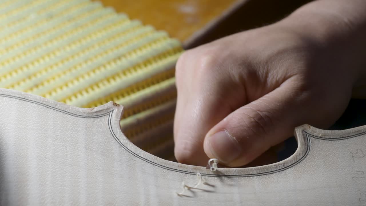 macro close up of artisan luthier maker work on new classic handmade raw violin smooth edge in waist and purfling rasp in workbench of workshop in Cremona Italy 4k video