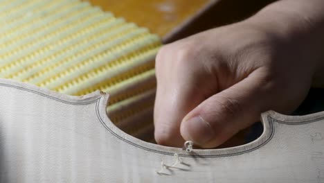 macro-close-up-of-artisan-luthier-maker-work-on-new-classic-handmade-raw-violin-smooth-edge-in-waist-and-purfling-rasp-in-workbench-of-workshop-in-Cremona-Italy-4k-video